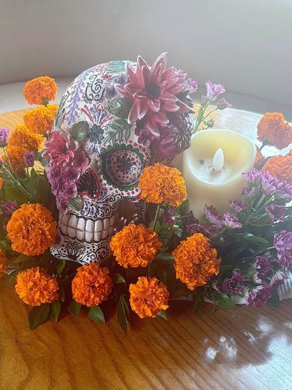 A beautifully painted sugar skull centerpiece, surrounded by marigolds, perfect for a Day of the Dead or Halloween theme.