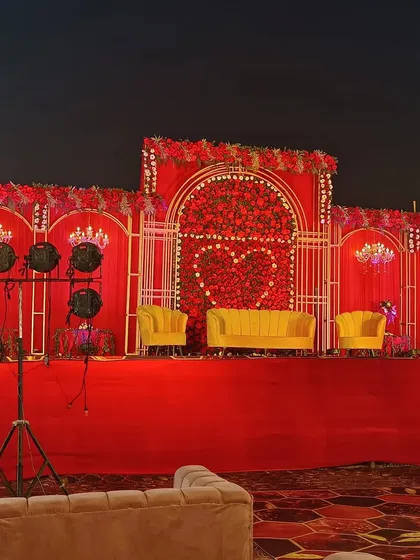 For a bold and royal wedding theme, I design grand stages like this one. It features a rich red floral backdrop with a heart motif, bright yellow velvet sofas for the couple, and dramatic lighting to create a memorable focal point.
