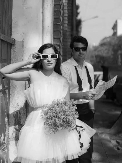 A cool, editorial-style black and white shot. Her quirky sunglasses and his classic look create a fun contrast, making this feel like a behind-the-scenes photo from a fashion magazine shoot.