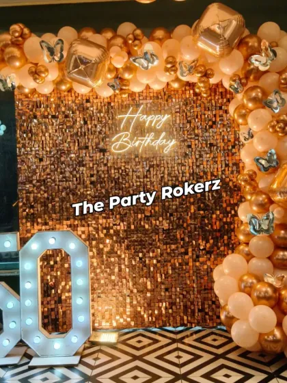 A closer view of the 50th birthday decor, highlighting the gold sequin wall and the elegant peach and gold balloon arch with butterfly details.