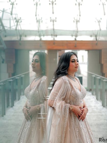 An artistic shot of the bride on her engagement day, using reflections to create a dreamy and contemplative portrait. This highlights her stunning lehenga and the beautiful ambiance of the venue.