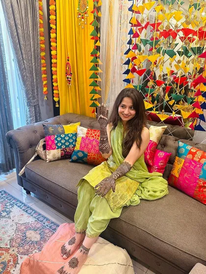 A client looking serene and beautiful at her home mehndi ceremony, surrounded by colorful and festive decorations.