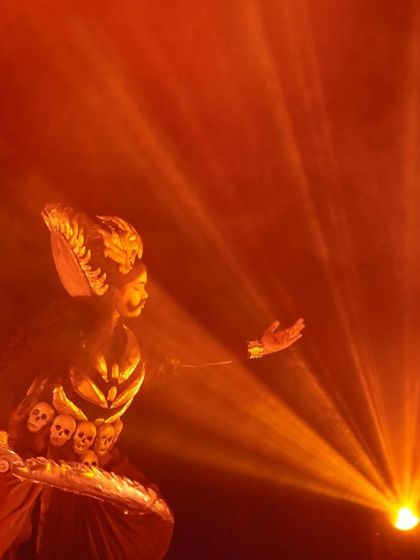 A character from "KRISHNA" is illuminated by a single, powerful beam of orange light, creating a dramatic and unforgettable stage presence.