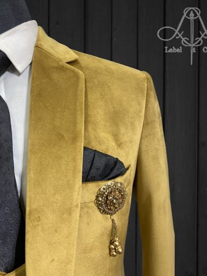 A close-up of the mustard velvet suit jacket. The elegant brooch and dark accessories create a beautiful contrast, highlighting the quality of the fabric and the attention to detail.