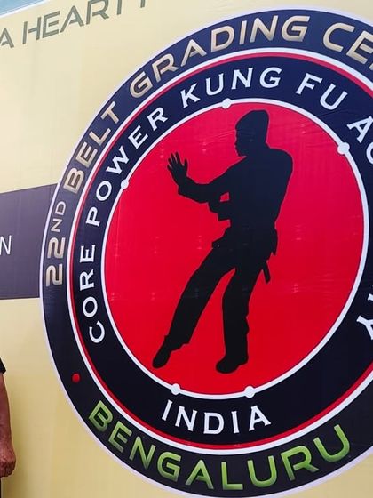 An instructor standing proudly before the banner at our 22nd Belt Grading Ceremony.