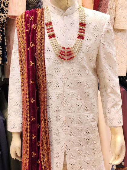 A close-up of a white sherwani with mirror work, paired with a maroon velvet stole. This is a classic look for a groom, combining elegance with a pop of rich color.