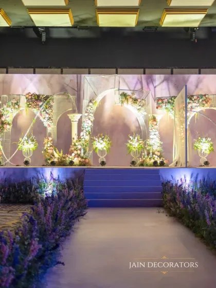 A stage designed to feel like a portal to a fairytale. A lavender-hued pathway leads to a series of ethereal arches adorned with pastel flowers, creating a dreamy and romantic setting for the couple.