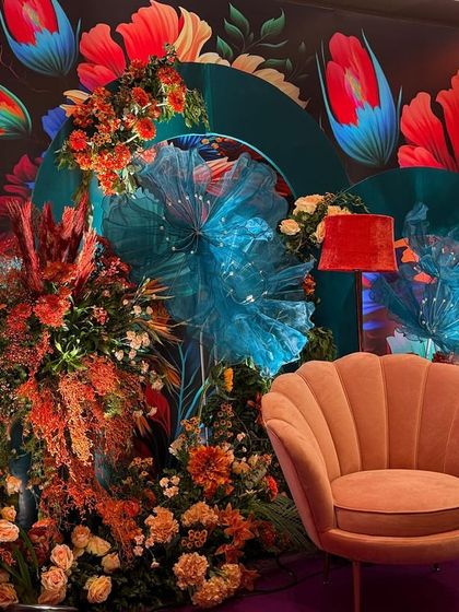 Another angle of the Bhaat ceremony decor, highlighting the mix of textures from the floral arrangements, the soft armchair, and the artistic backdrop. The lighting enhances the vibrant colors, making the space feel alive.