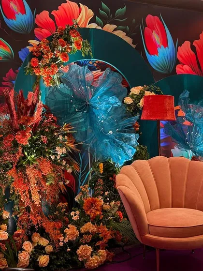 Another angle of the Bhaat ceremony decor, highlighting the mix of textures from the floral arrangements, the soft armchair, and the artistic backdrop. The lighting enhances the vibrant colors, making the space feel alive.