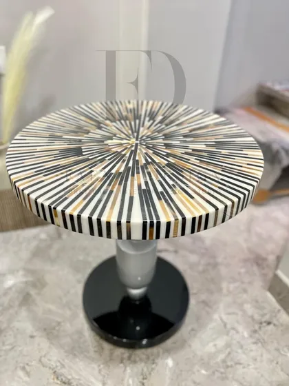 A side table featuring a striking sunburst-patterned inlay top. The combination of black, white, and gold tones on a classic pedestal base creates a piece that is both artistic and functional.