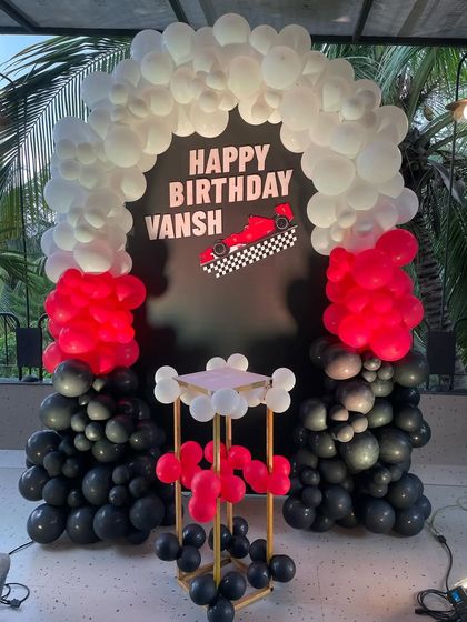 A high-speed race car themed birthday party. This decoration features a striking black, red, and white balloon arch over a custom backdrop with a Formula 1 car, perfect for any young racing fan.