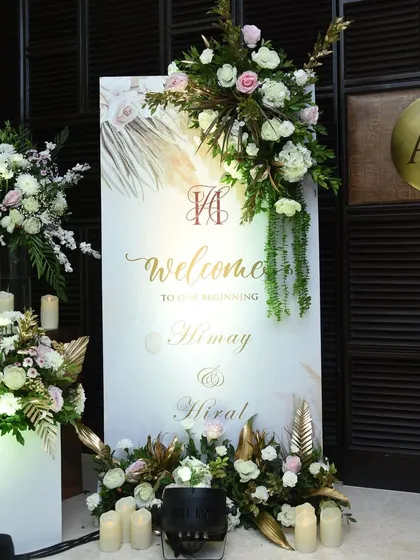 A sophisticated welcome sign for Almay and Hiral, featuring their monogram and elegant calligraphy, framed by arrangements of white roses and gilded leaves.