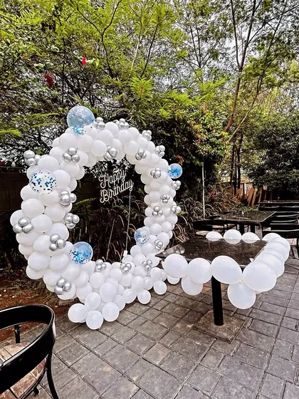 A white and silver balloon ring set up for an outdoor party. This decoration creates a beautiful contrast with the surrounding greenery.