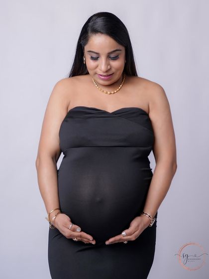 A simple and heartfelt solo portrait. The mom-to-be looks down at her bump with love, captured against a clean, minimalist background.
