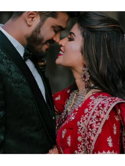 A close-up shot capturing the romance. The groom's dark green tuxedo and the bride's traditional red lehenga create a rich, cinematic look for any wedding album.