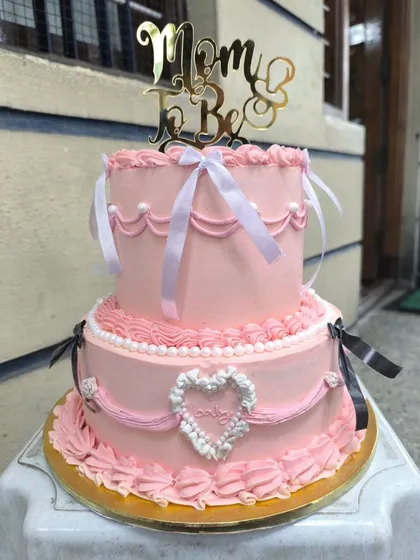 Coquette and cute. This super frilly two-tier baby shower cake was made in the beautiful Lambert style, with delicate piping, ribbons, and a sweet heart detail for the mom-to-be.