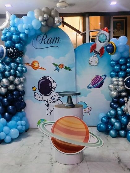 An out-of-this-world space and astronaut themed birthday party. The setup includes planet cutouts, a rocket, and a balloon arrangement in shades of blue and silver.