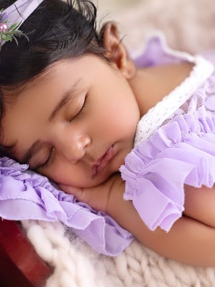A close-up of a sleeping newborn girl in a lovely lavender dress. Her delicate features and peaceful expression are the focus of this shot.