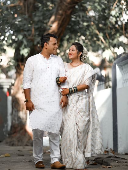 A candid shot of a couple in all-white attire, likely from a Buddhist or Nirankari wedding, walking together and sharing a happy moment.