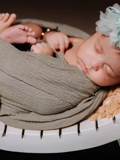 A close-up of a sleeping newborn, swaddled and resting on a curved white prop, highlighting their delicate features and tiny toes.