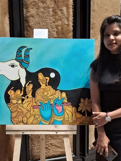 An artist with her painting that creatively combines the silhouette of a cow with scenes of Krishna.