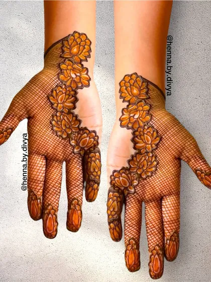 A modern and artistic take on floral mehendi. This design uses a fine net pattern as a base for a trail of bold, beautiful lotus flowers climbing up the hand.