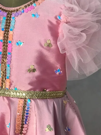 A close-up of the delicate, iridescent sequins and ruffled tulle sleeves on the pink peplum top, details that make each piece feel special.