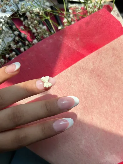 It's all in the details. This close-up shows a classic white French tip manicure with a delicate, hand-sculpted 3D bow accent, adding a touch of sweetness to an elegant design.