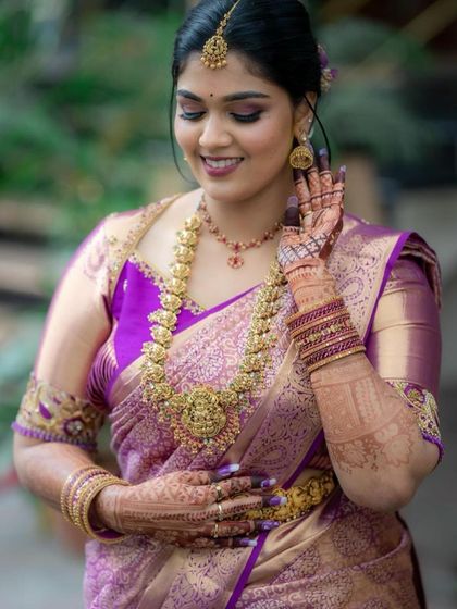 A stunning South Indian bride, her hands adorned with mehendi, adjusting her traditional gold jewelry.