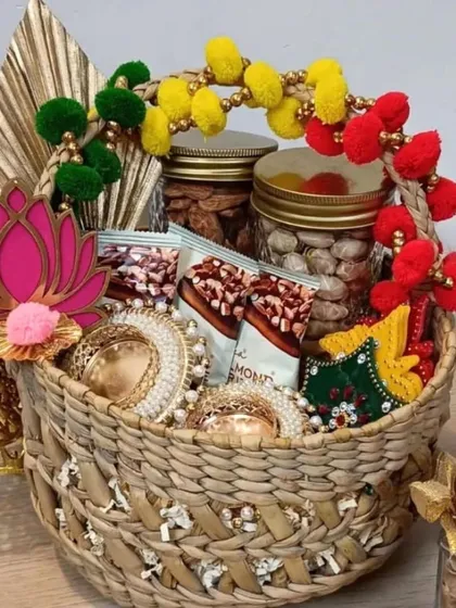This vibrant hamper is packed in a sustainable kauna grass basket. It's filled with traditional Indian decor like pearl-studded diyas, a lotus cutout, and pom-pom garlands, alongside jars of healthy snacks for a complete festive feel.