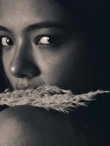An intimate close-up where the pampas grass is used to create a soft, textured frame. The focus on the model's eye and the shallow depth of field make this a very personal and engaging black and white shot.