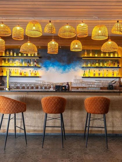 For this bar, we used a warm and inviting color palette with orange quilted bar stools and a cluster of cane pendant lights. The design creates a cozy and cheerful atmosphere, perfect for a relaxed evening.