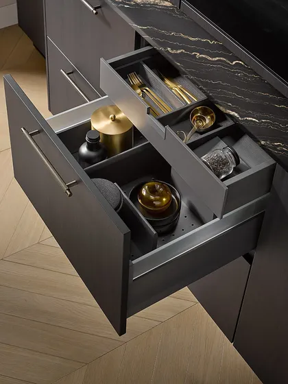 A two-tier drawer organizer with custom compartments for cutlery and cooking tools, all finished in a sophisticated dark ash to match the kitchen's exterior.
