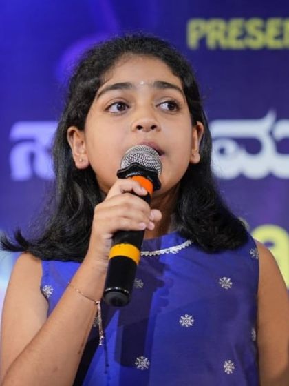 Pranathi Kumar, a student of Smt. Gayathri Mohan, sings into the microphone during her performance.