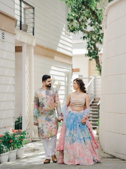 The couple takes a romantic stroll, holding hands. Their colorful Mehendi outfits and the charming setting make for a beautiful pre-wedding portrait.