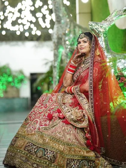A regal portrait of the bride seated, with her hand gently touching her face. The green background lighting adds a touch of modern glamour.