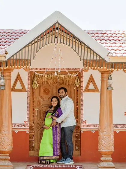 A wide shot capturing the couple standing before the entrance of a beautifully decorated traditional home.
