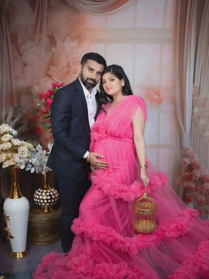 A sweet couple's maternity photo, with the father-to-be embracing his partner who is wearing a beautiful pink ruffled gown.