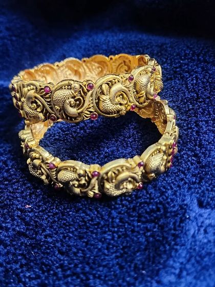 A pair of antique-finish bangles with intricate fish motifs and kemp stone detailing. Renting bangles is a great way to add more detail to your look without the expense.