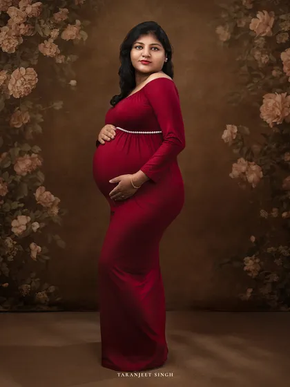 Standing against a beautiful floral backdrop, this mother-to-be in a classic red gown is the picture of elegance. The painted background adds a layer of artistry to the portrait.