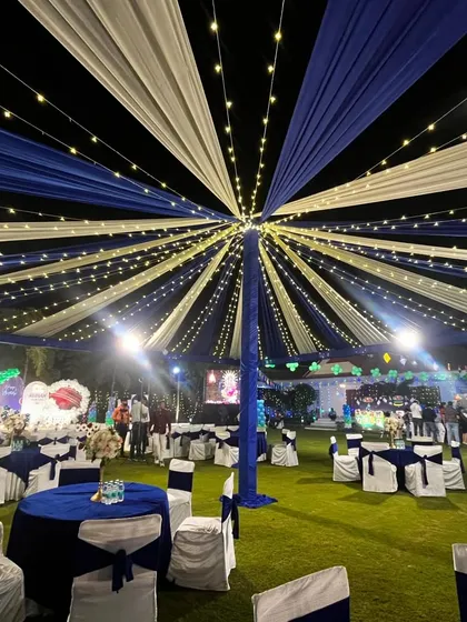 A wider view of the blue and white tent, showing the spacious lawn setup for a large gathering.
