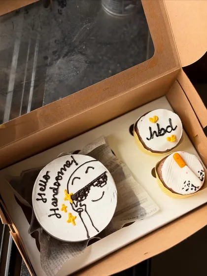 A cool and fun birthday set with a "Hello Handsome!" bento cake featuring a cartoon character in sunglasses. The two accompanying cupcakes are also decorated with fun, simple designs.