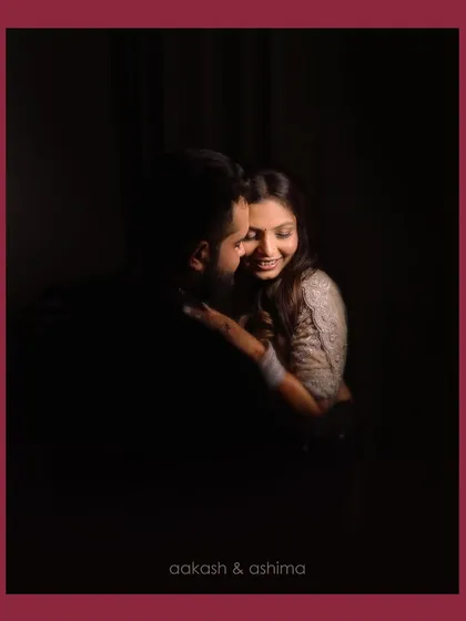 A close, intimate portrait of a couple in a dark setting, with soft light highlighting their smiles and connection.