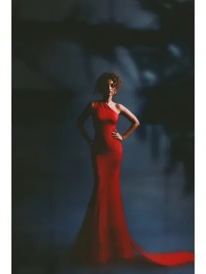 A classic studio shot of a woman in red. The styling is pure Hollywood glamour, with a figure-hugging red gown and a powerful stance against a moody, textured background.