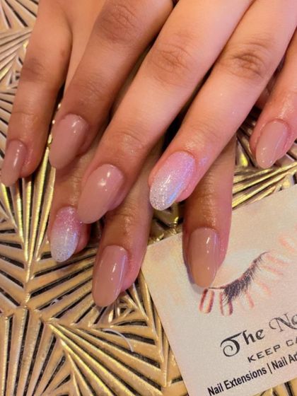 Nude almond-shaped nails with a subtle touch of sparkle. The ring and pinky fingers are accented with a beautiful silver-to-white glitter ombre effect.