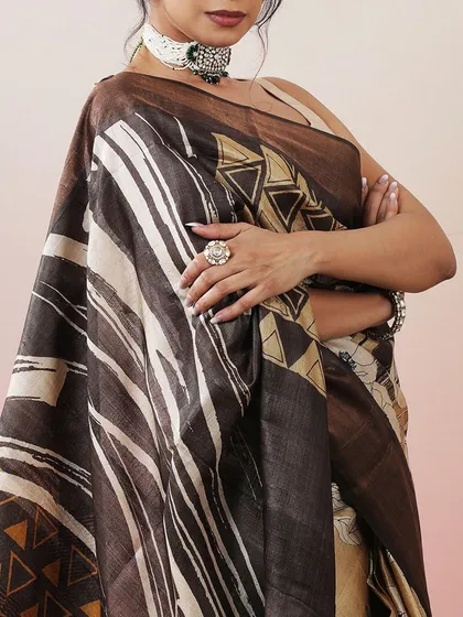 A close-up of a contemporary printed saree in earthy tones of brown and beige, with geometric patterns.