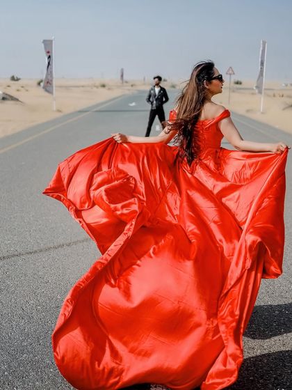 A dynamic and powerful shot on a Dubai road. The bride's flowing red gown creates a sense of movement and drama, with her partner in the background, telling a story of anticipation and modern romance.