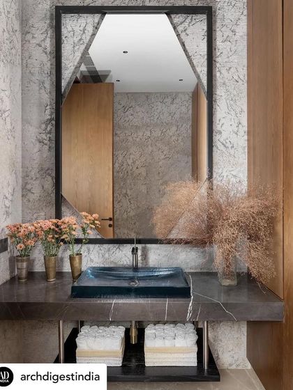 This powder room in the K Residence, featured in Architectural Digest, uses dramatic stone and a custom geometric mirror to create a powerful statement. The deep blue glass basin adds a pop of colour and a touch of artisanal beauty.