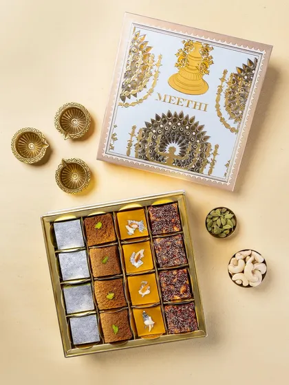 A top-down view of a festive mithai box from Meethi India, accompanied by diyas and dry fruits. This angle is effective for showcasing the complete product offering.