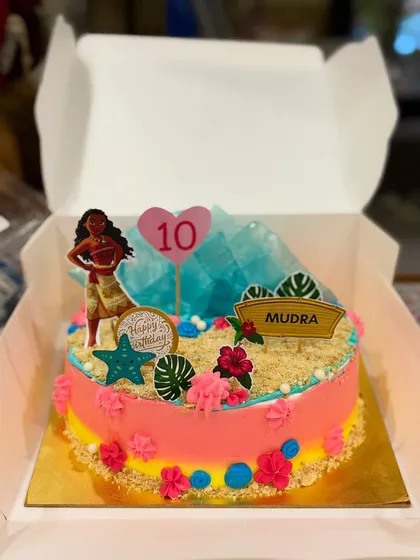 A Moana themed cake for a 10th birthday. It's decorated with edible sand, tropical flowers, and character toppers to create a scene straight from the movie.